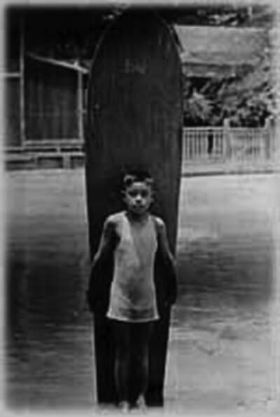 Interviewee Minoru Aoki stands in Hamohamo Stream (no longer in existence) with surfboard, Waikiki, ca. 1920s. (Photo courtesy Minoru Aoki.)